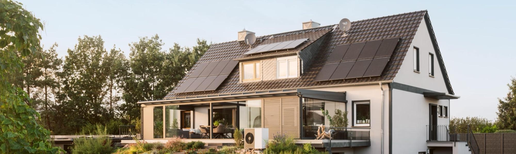 Einfamilienhaus mit Solaranlage auf dem Dach und Wärmepumpe im Garten