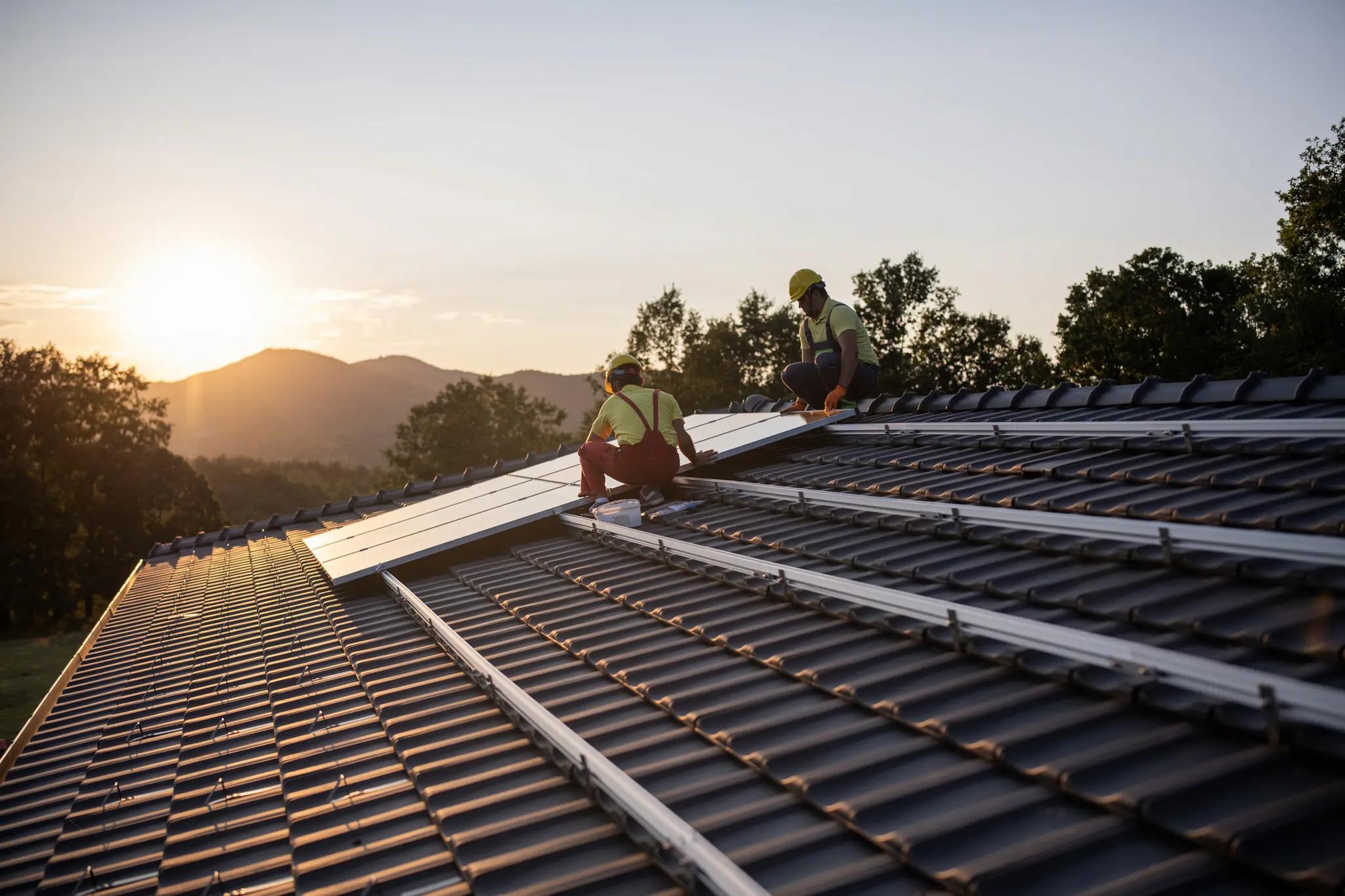Zwei Monteure befestigen Solarmodule auf einem Schrägdach